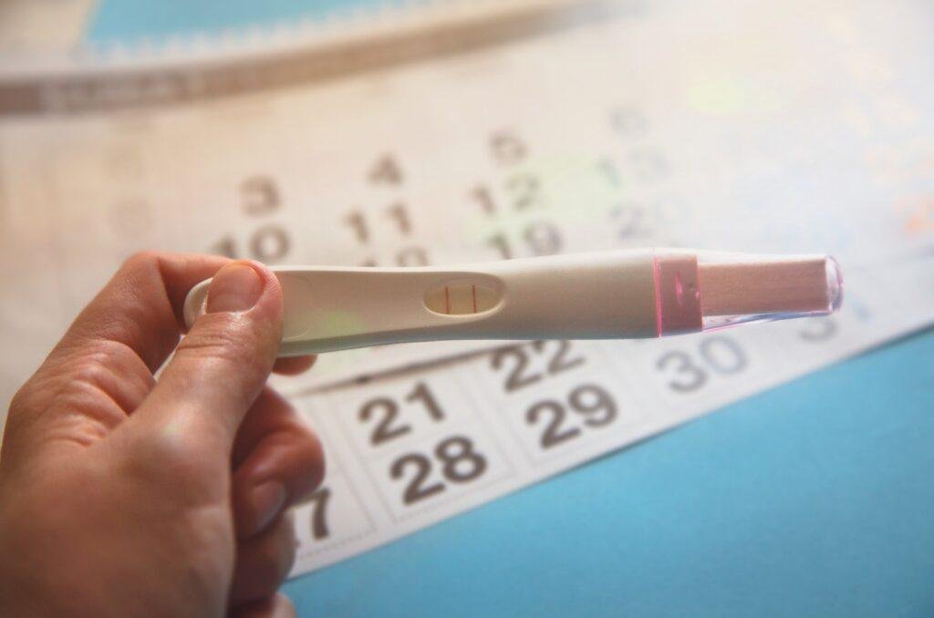 A women holding a positive pregnancy test in front of a calendar